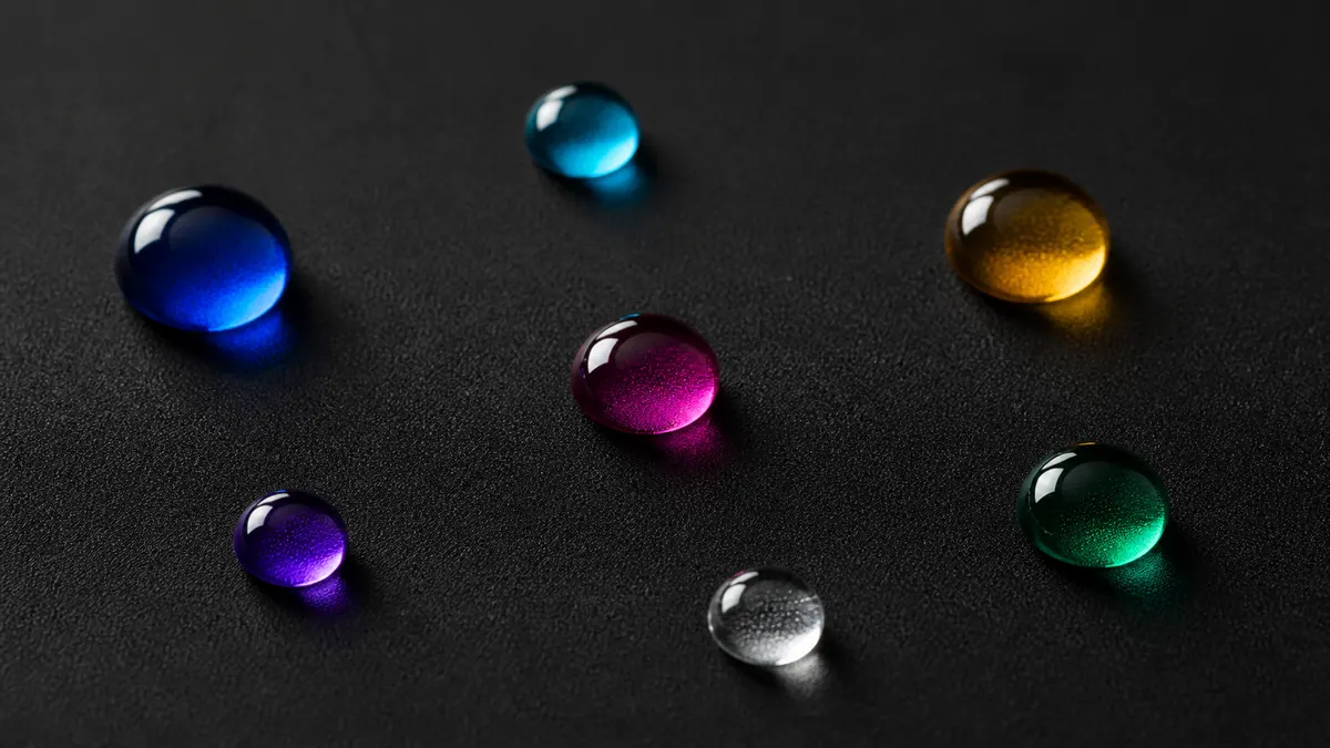 Seven jewel-toned water beads sit apart on a charcoal water-repellent membrane.