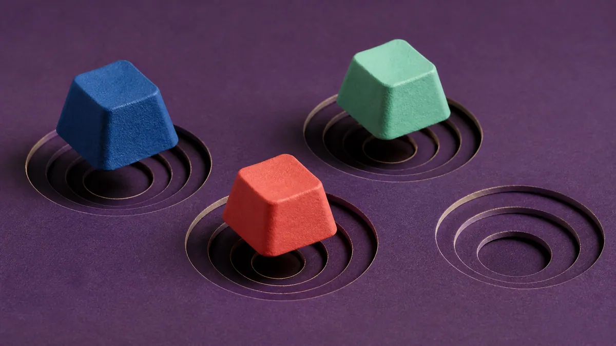 Three blank molded-paper keycaps hover above layered circular wells beside one empty well on an aubergine surface.