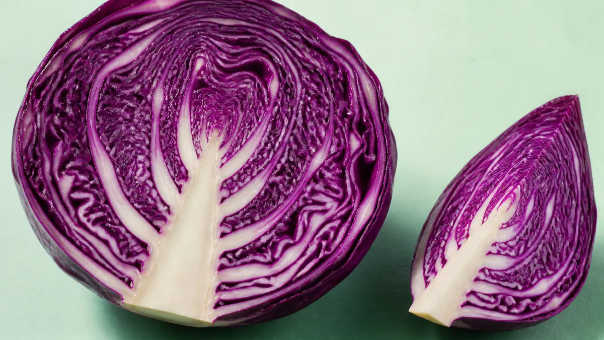 A red cabbage half and wedge show tightly layered purple leaves and pale branching ribs on a mint-green surface.
