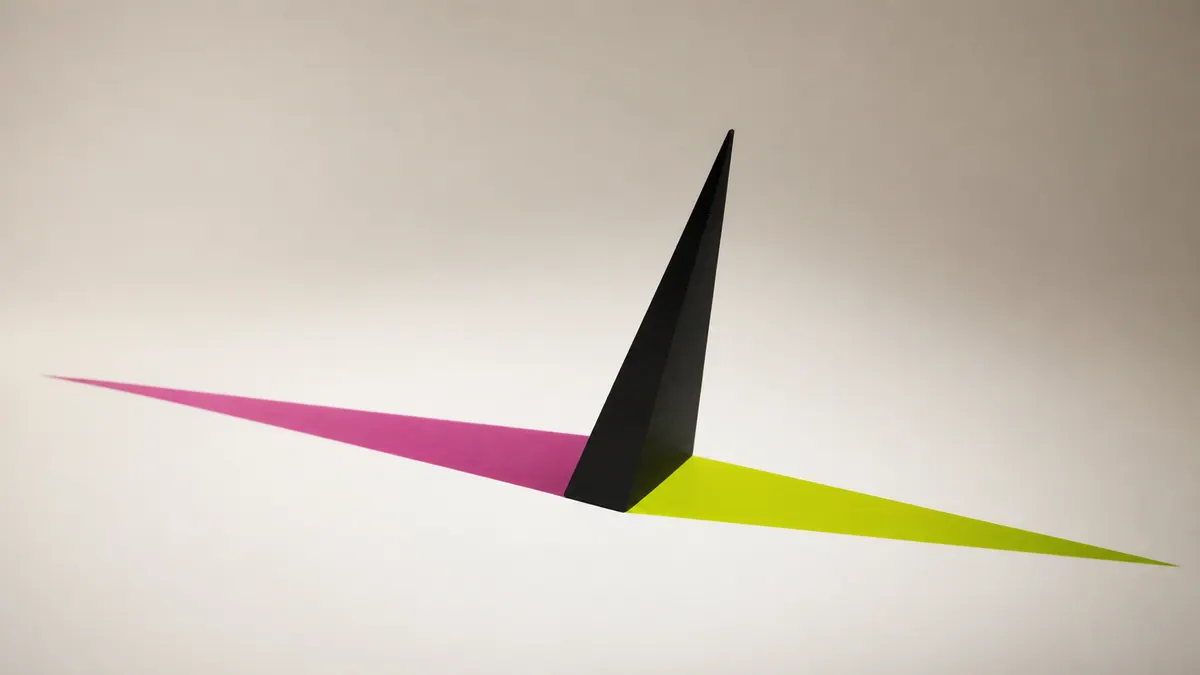 A matte-black gnomon casts separate chartreuse and magenta shadows across a seamless bone-white surface.