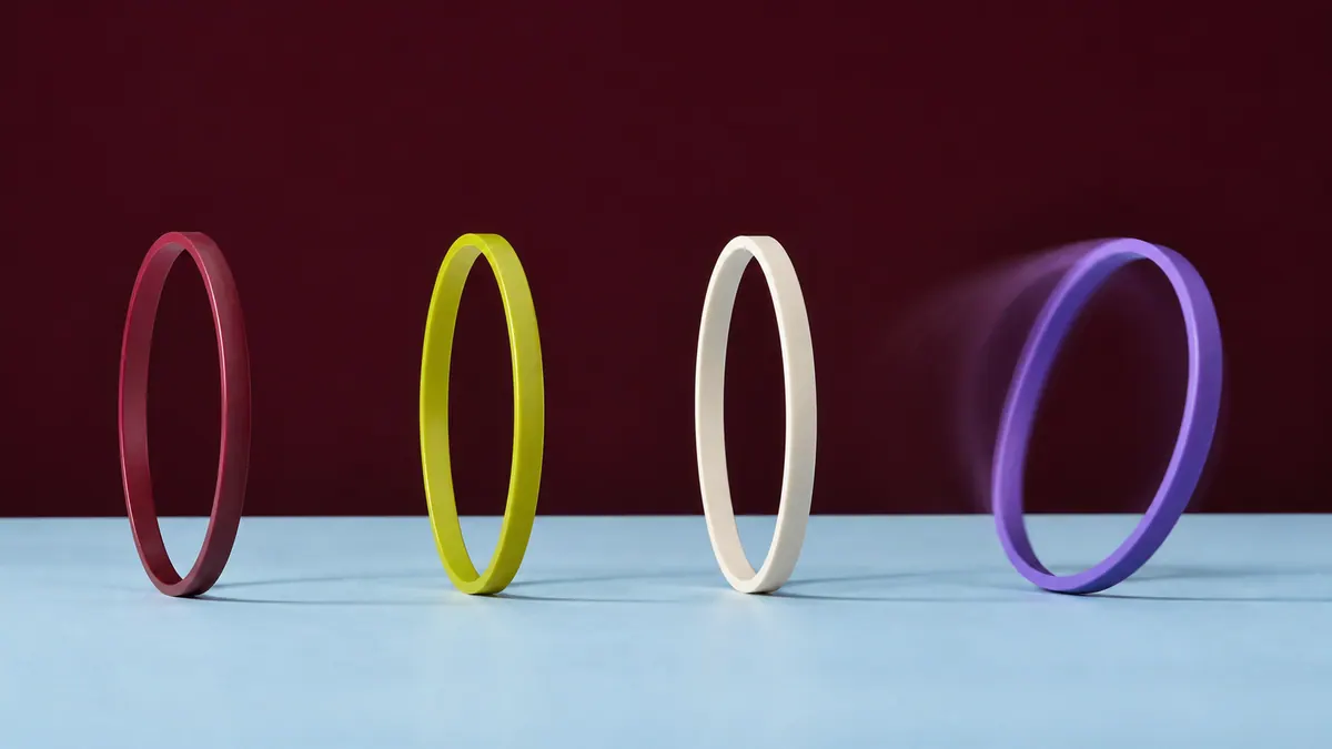 Three colorful rings stand upright while a fourth wobbles across a pale-blue studio surface.