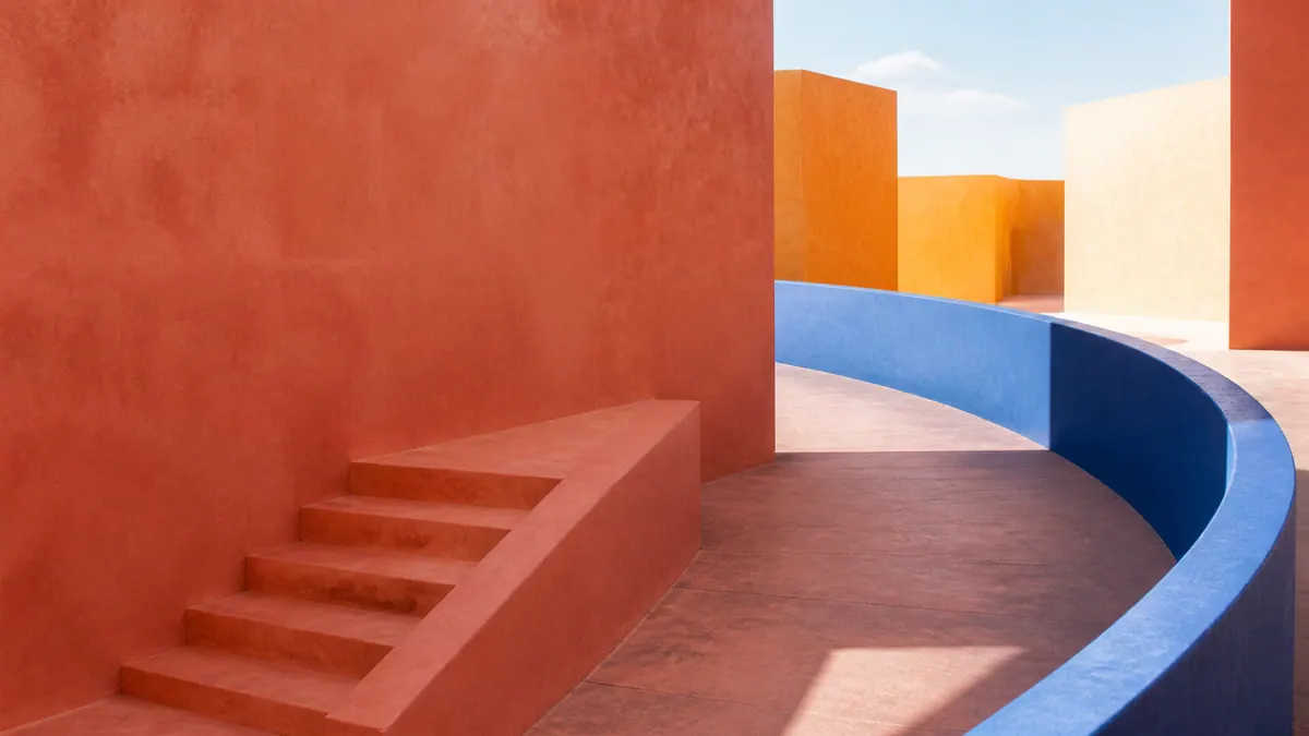 A coral staircase stops at a solid terracotta wall while a broad cobalt ramp curves into an open saffron courtyard